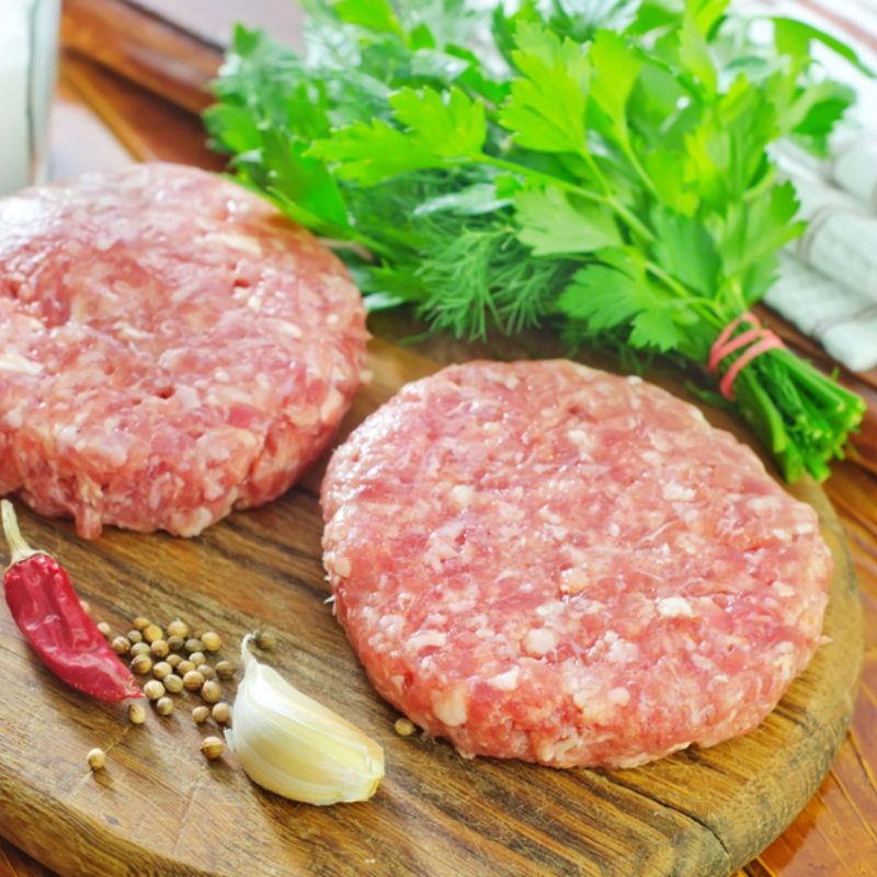 Two raw burgers on a board with garnish from our Coorie Retreats meat boxes.