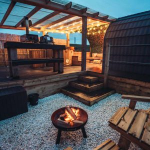 The outdoor area lit up at night and a fire pit at Portside Pasture glamping pod at Coorie Retreats